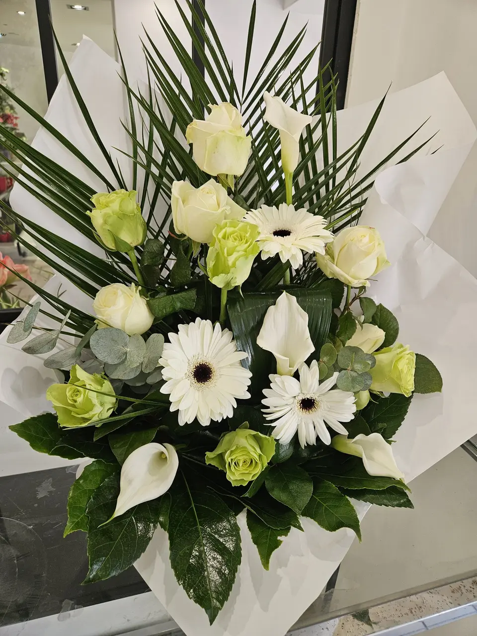Bouquet blanc et vert de roses, gerberas et arums dans un papier blanc