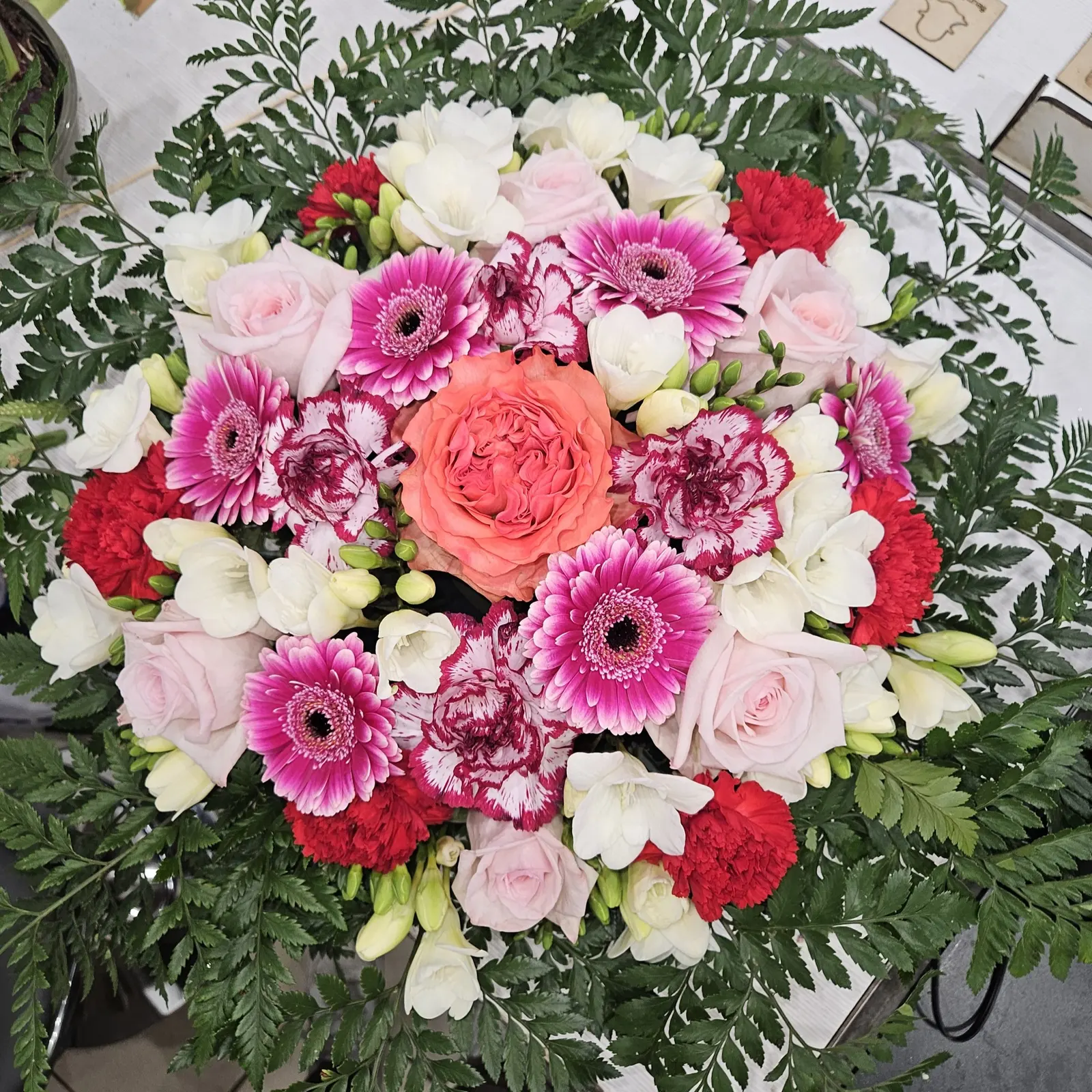 Bouquet rond de gerberas roses, roses saumon et fleurs blanches sur feuillage de fougère