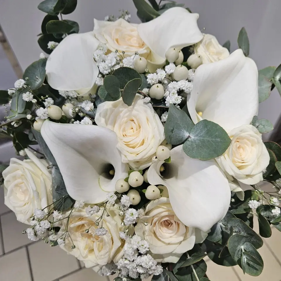 Bouquet de mariée rond tout blanc : arums, roses crème, gypsophile et symphorine sur feuillage d'eucalyptus