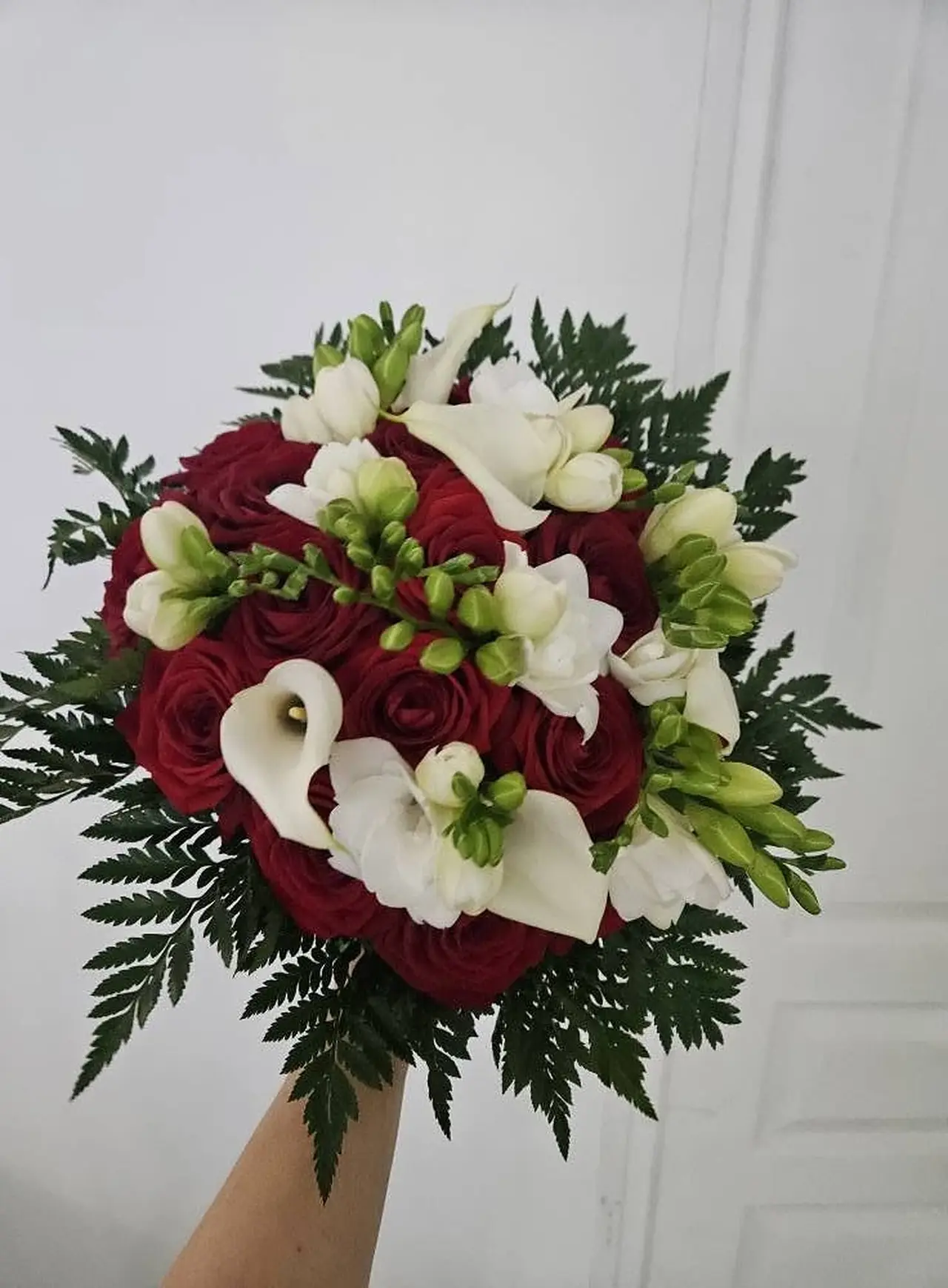 Bouquet de mariée rond : roses rouges, callas blancs et freesias sur fougère