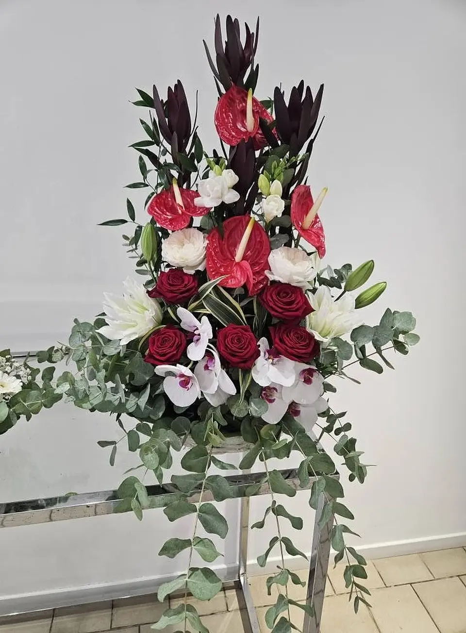 Composition de cérémonie en hauteur : anthuriums, roses rouges, orchidées et eucalyptus retombant