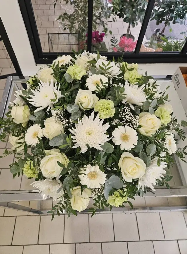 Coussin rond de deuil blanc et vert : roses, gerberas, chrysanthèmes et eucalyptus